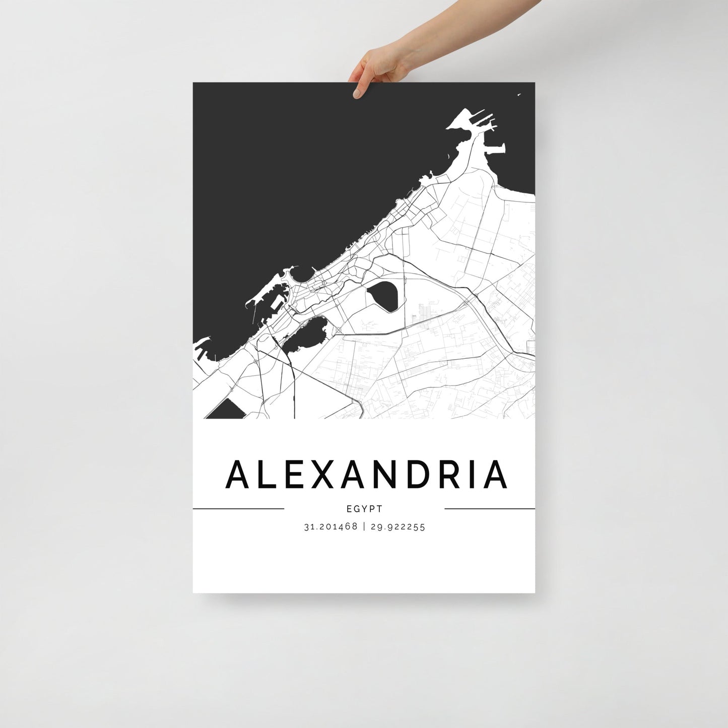 A person admires the stunning Alexandria Map by FN Prints, with its black and white design elegantly capturing the historic city's streets and coastal outline. This minimalist masterpiece, complete with geographic coordinates, stands out as timeless black and white wall art.