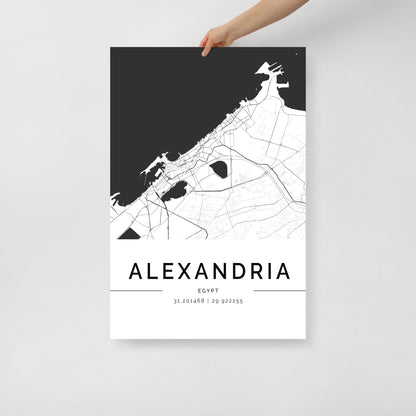 A person is holding an FN Prints Alexandria City Map, a stunning piece of black and white wall art. It beautifully showcases the historic streets and landmarks with intricately detailed roads and waterways. The coordinates 31.201648, 29.922255 are subtly displayed below the city's name, adding a modern flair to this timeless design.