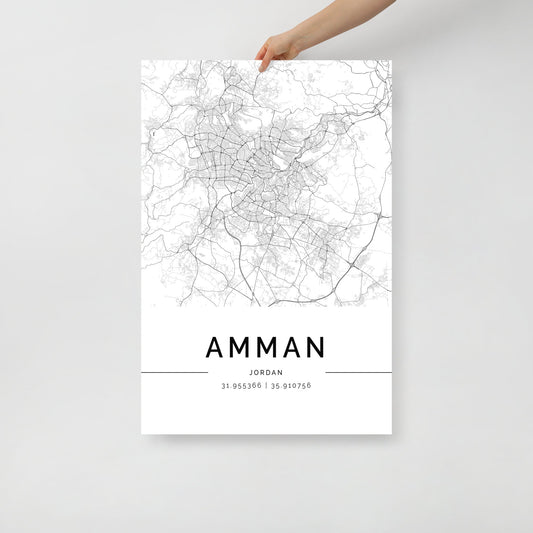 A hand holds a poster featuring the Amman Map by FN Prints, beautifully capturing the intricate black and white details of Jordan's capital. Displaying geographical coordinates 31.95356° N, 35.91076° E, it highlights roads and topographical features with touches of Middle Eastern architecture.