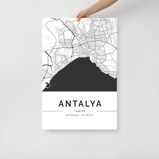 A hand holds an FN Prints Antalya Map poster, a minimalist black and white design perfect for wall art. It highlights the city's streets and coastal areas and celebrates its cultural heritage with coordinates displayed at the bottom.