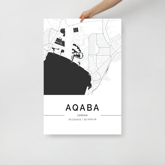 A person holds an Aqaba Map by FN Prints, a minimalist black and white poster expertly designed to complement modern décor. The map highlights the streets and coastal area, making it perfect for striking wall art. Coordinates at the bottom, 29.534443 | 35.006118, add charm to this elegant map print.