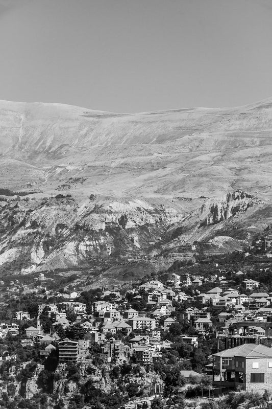 A black and white image entitled "Ariz, Lebanon" by FN Prints captures the natural grandeur of a mountainous landscape, with scattered buildings. The background features steep, rugged mountains, while the foreground reveals a densely packed cluster of houses and structures.