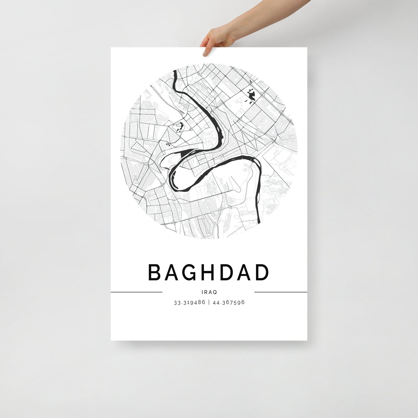 A hand displays the stunning "Baghdad Map" wall art print by FN Prints, showcasing a black and white circular map of Baghdad's layout with its river elegantly unfolding. Coordinates are printed below, beautifully capturing the historic landmarks of Baghdad, Iraq.