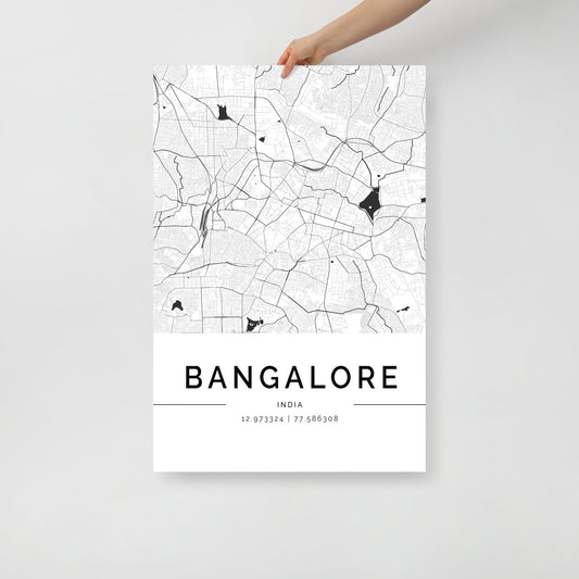 A person holds a Bangalore Map, an intricately designed black-and-white wall art print by FN Prints, highlighting the city's streets and landmarks. Below the city name, the coordinates 12.973324, 77.586308 are elegantly displayed on this eye-catching map poster.