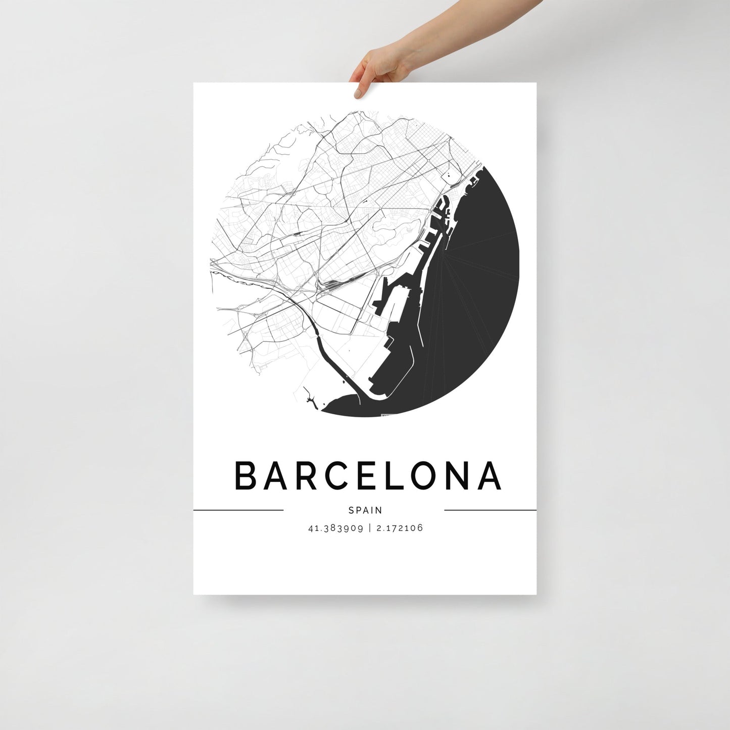 A person holds a FN Prints Barcelona City Map, a minimalist black and white wall art poster. The circular map showcases architectural beauty print elements and features the geographical coordinates below the city's name.