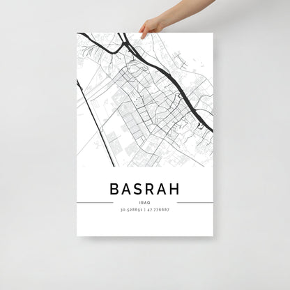 A hand holds the Basra Map by FN Prints, showcasing a monochrome depiction of the city's layout with geographic coordinates 30.528651, 47.776687 below. This minimalist wall art captures the street and road design, offering a glimpse into Middle Eastern history.