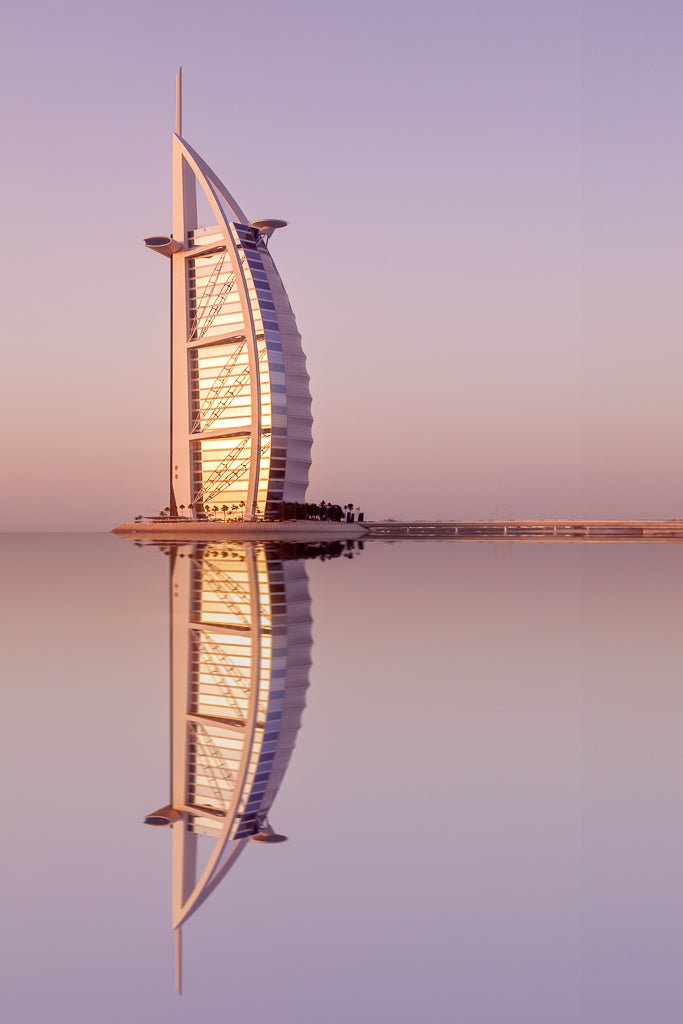 The "Burj Al Arab: Dubai" print by FN Prints beautifully captures the luxurious hotel standing majestically on an artificial island, resembling a sail and perfectly reflecting on calm water during a serene sunset sky. The scene, bathed in shades of pink and purple, makes it an ideal piece to showcase the tranquility of Dubai.