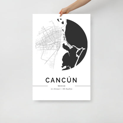 A hand holds a FN Prints Cancun City Map Wall Art Print in black and white. The poster elegantly showcases the city's street layout in a circular design, with geographic coordinates 21.174292, -86.846531 printed below, making it an elegant addition to any space.