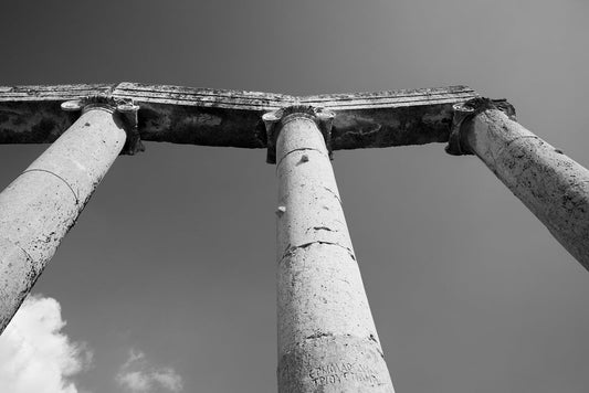Black and white fine art photography looking up at three ancient Roman columns and a stone archway in Jerash, Jordan.