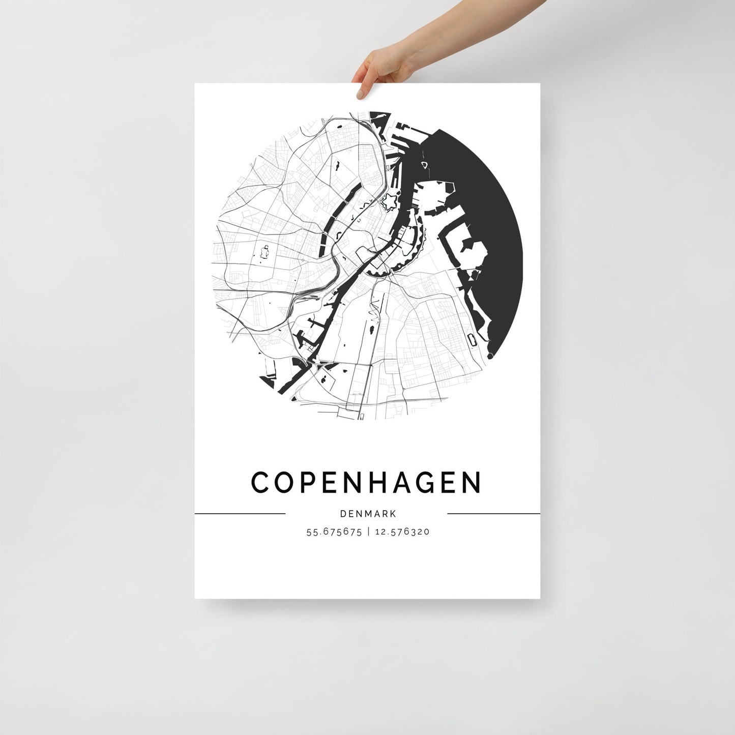 A person holding an FN Prints "Copenhagen Map" poster, showcasing a black and white city map with Scandinavian elegance. The wall art print features geographical coordinates (55.675675, 12.576320) and prominently displays "Copenhagen" in bold beneath the intricately detailed map.