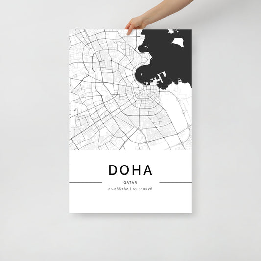 A person is holding the FN Prints' Doha City Map, a black and white minimalist wall art poster that beautifully showcases the intricate layout of Doha with its roads and coastal lines. This poster features the geographic coordinates 25.286782, 51.530926 at the bottom—making it an ideal piece for those who appreciate Qatar's unique charm.