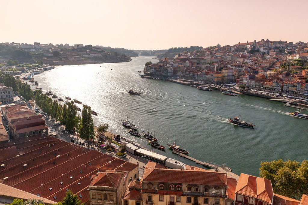 Experience the breathtaking beauty of the Douro River Porto with this stunning photograph by FN Prints. Capturing the winding river through a vibrant cityscape, you'll find boats gracefully sailing on the water. Both riverbanks are adorned with charming red-roofed buildings and lush greenery, highlighting the area's historic architecture. The setting sun casts a warm, golden light that reflects off the water's surface, making this Porto waterfront scene truly captivating.