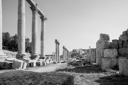 Black and white fine art photography of a row of tall Corinthian columns along an ancient paved street in the ruins of Jerash, Jordan.