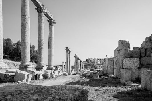 Black and white fine art photography of a row of tall Corinthian columns along an ancient paved street in the ruins of Jerash, Jordan.