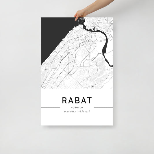 A hand holds an FN Prints Rabat Map, showcasing a black and white depiction of Rabat, Morocco. This wall art print includes the geographic coordinates: 34.0049531, -6.852376.