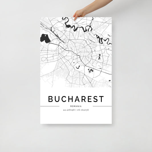 An individual holds a black and white FN Prints Bucharest Map wall art print. This minimalist poster features intricate streets and landmarks of Bucharest, Romania, with its geographical coordinates stylishly displayed at the bottom on a simple background.