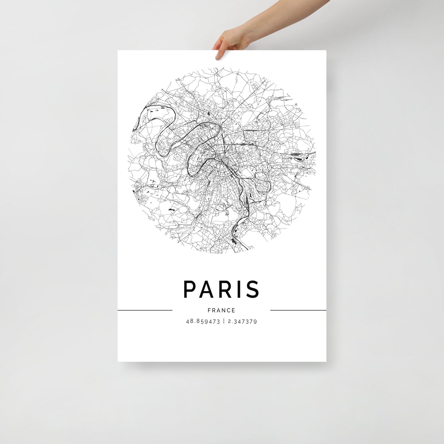 A person's hand holds an FN Prints Paris Map poster, printed on premium-grade paper. This black and white wall art showcases intricate street details, with the coordinates "48.856973 | 2.341379" elegantly displayed below.