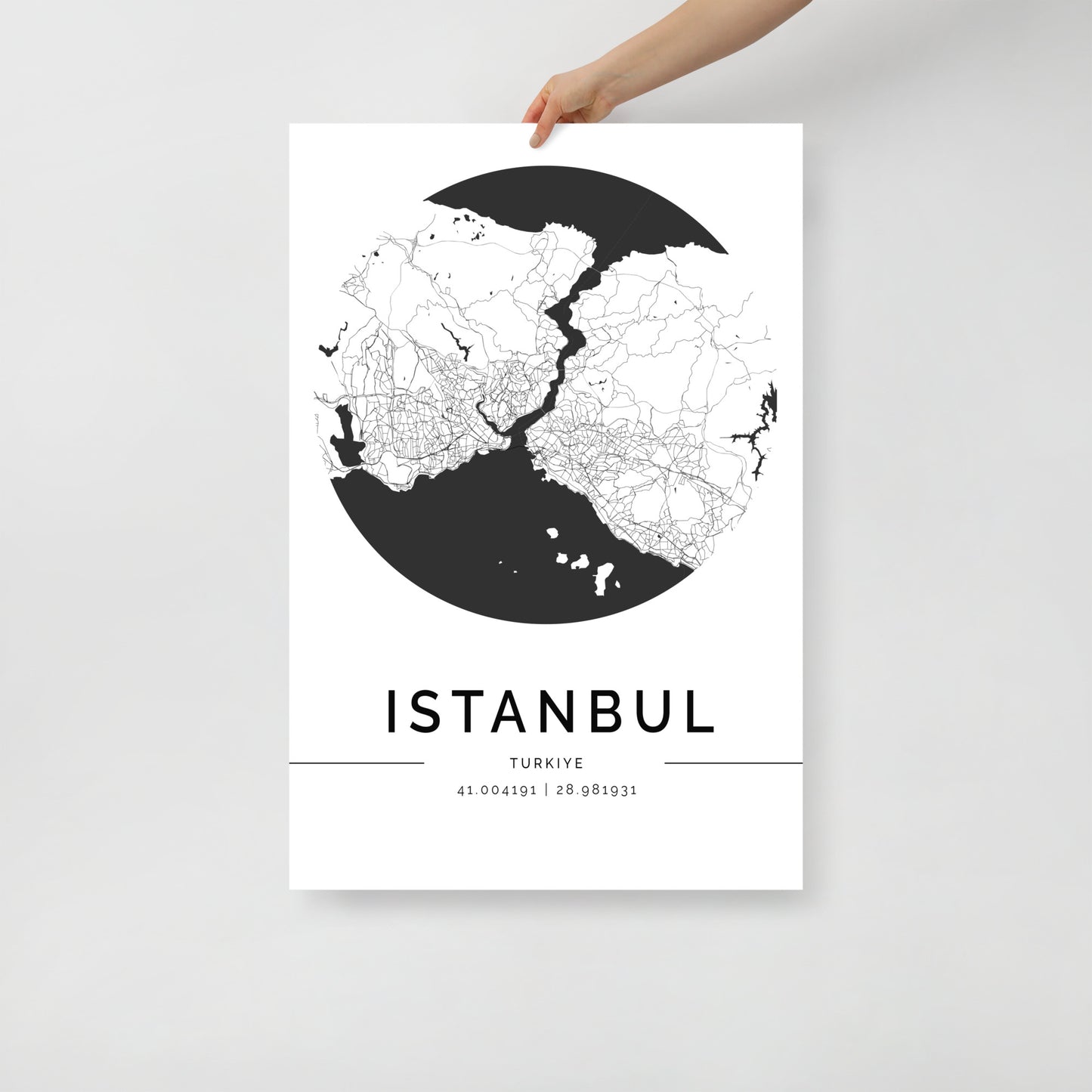 A hand displays a captivating Istanbul Map poster by FN Prints, featuring a minimalist black and white design that intricately highlights the streets and neighborhoods of the city, capturing its architectural beauty. The coordinates 41.00419 | 28.987931 elegantly adorn the area below the city name.