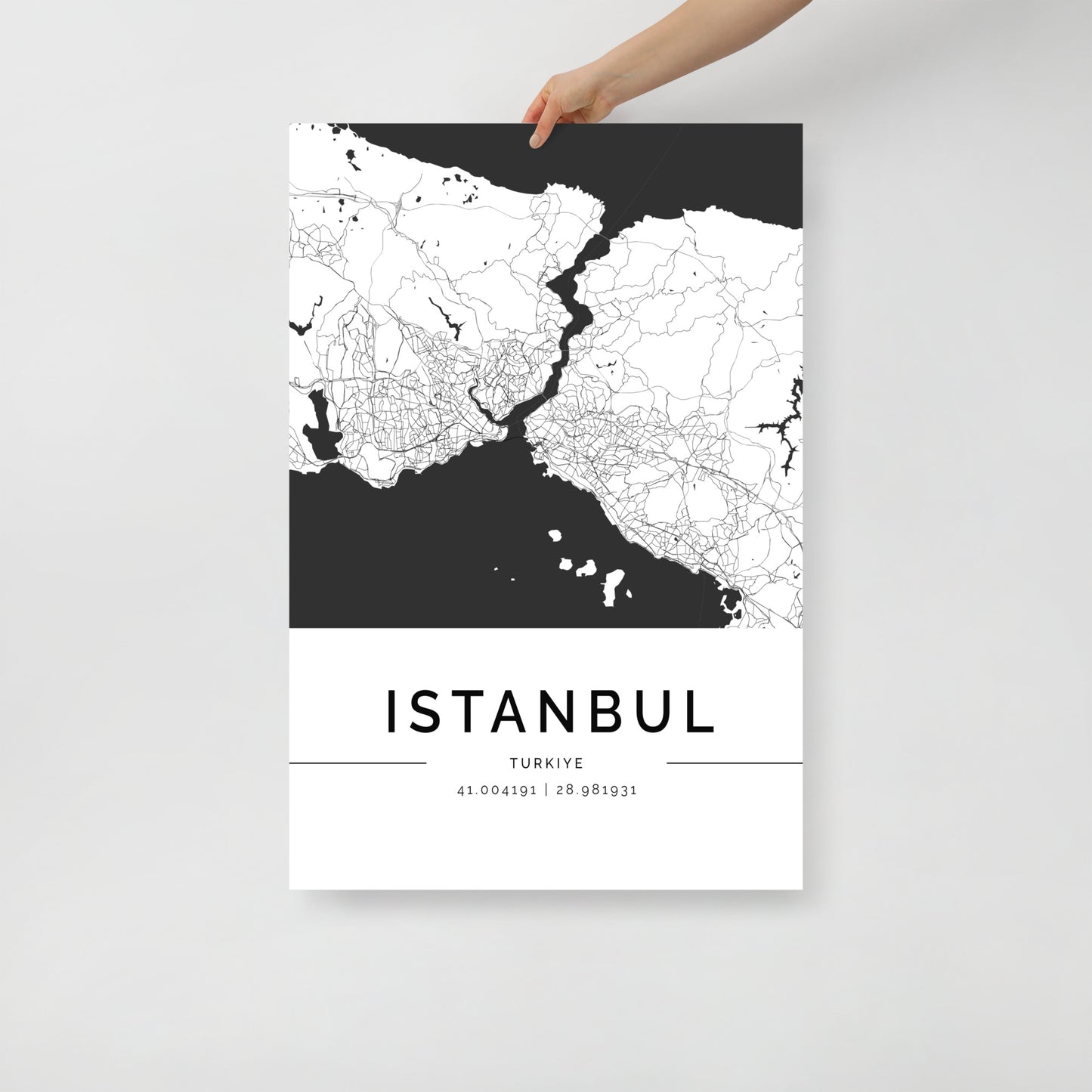 An individual holds an exquisite black and white FN Prints Istanbul Map poster, highlighting the city's intricate street designs. The waterway elegantly splits the city, emphasizing its architectural splendor. At the bottom, the coordinates 41.00419°N, 28.987931°E are beautifully presented.