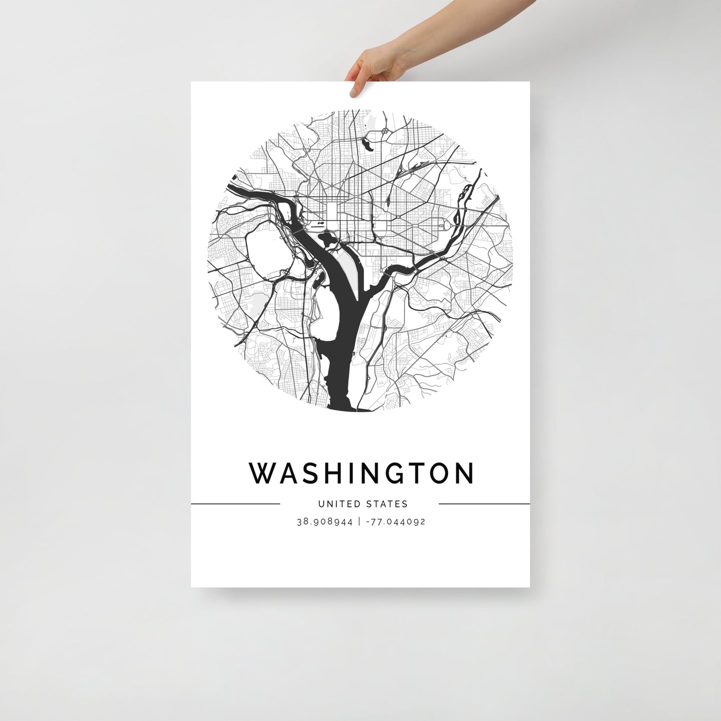 A person is holding a Washington Map poster from FN Prints, designed in black and white with a circular layout showcasing detailed streets, rivers, and iconic landmarks. Historic monuments are highlighted on the map, with the coordinates 38.90844, -77.044092 elegantly displayed below.