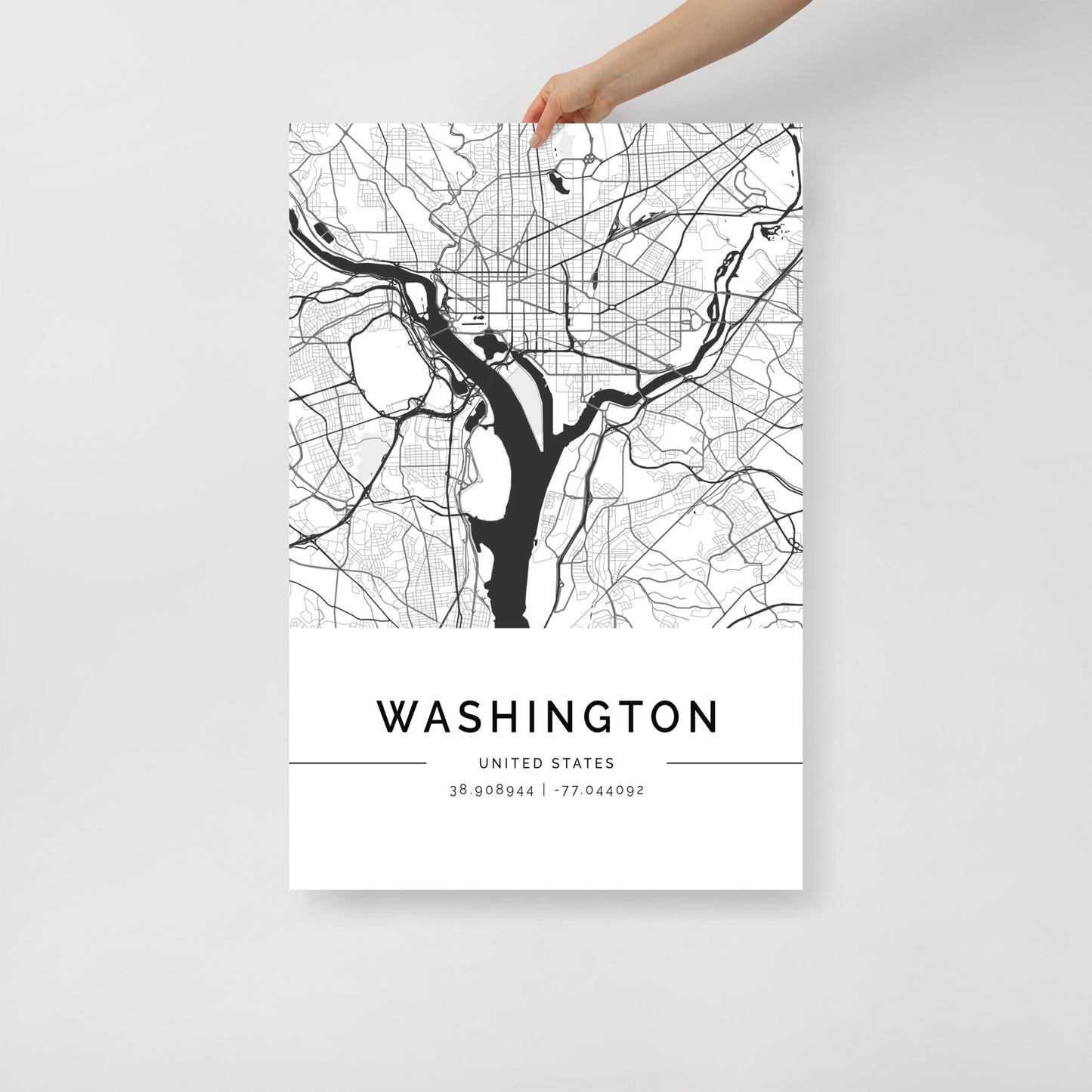 A hand holds a FN Prints' Washington Map poster, elegantly highlighting the city's iconic landmarks and coordinates 38.908844, -77.044092 on a minimalist light gray background.