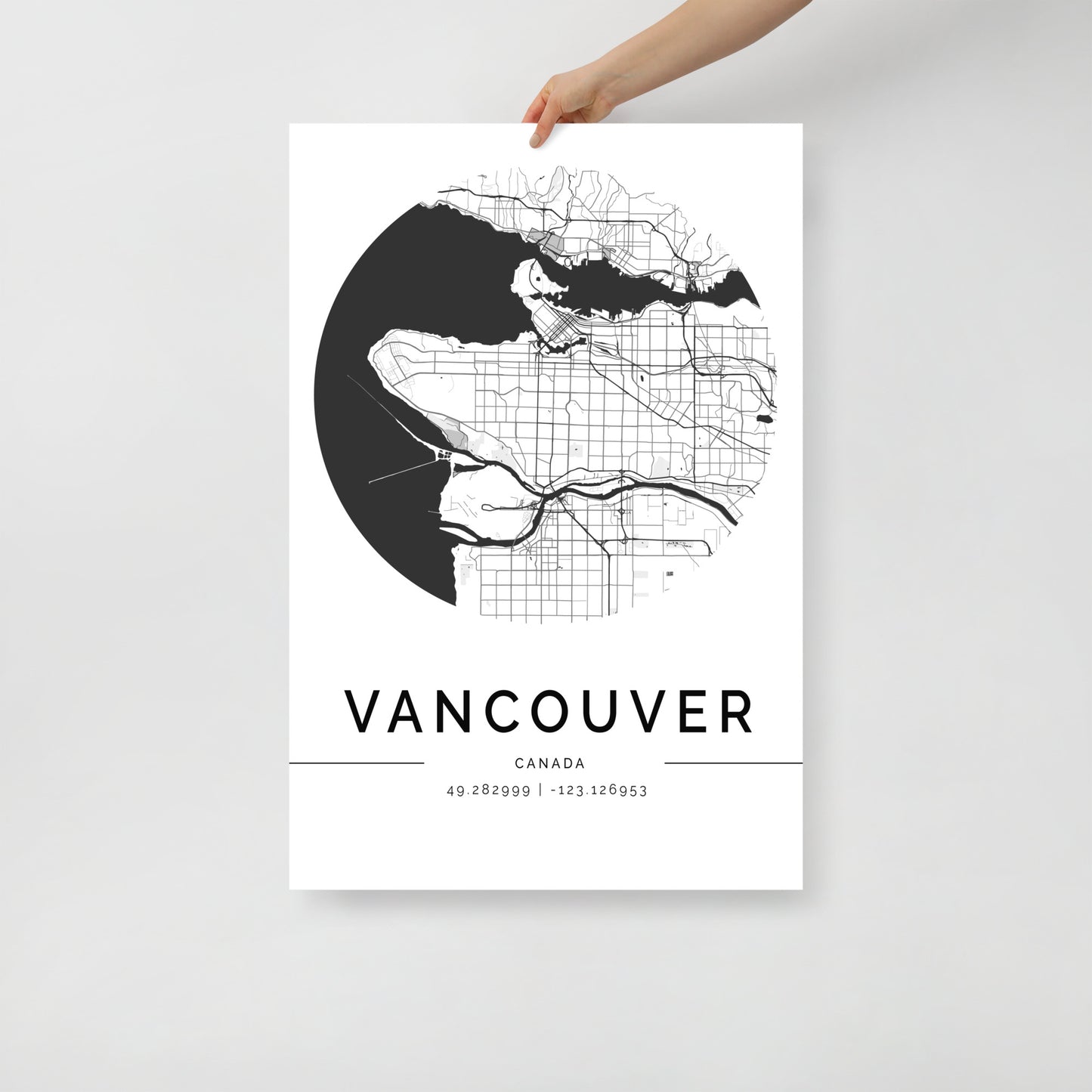 A person holds the FN Prints Vancouver Map, a minimalist black and white poster that displays the city's detailed street layout and geographic coordinates, set against a plain background. This elegant cityscape print is an ideal piece of black and white wall art for any decor style.