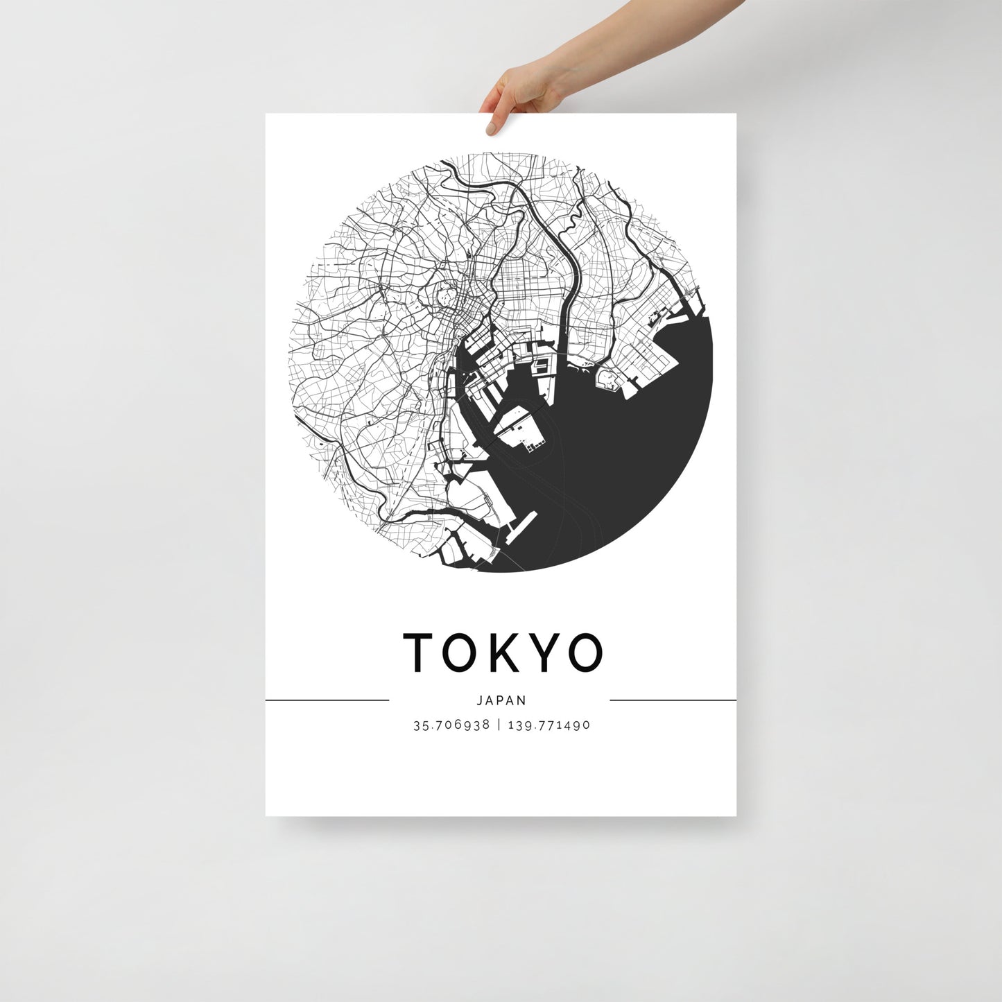 In someone's hand is a striking black and white Tokyo map print by FN Prints, showcasing the city's intricate grid of streets and waterways. This poster includes the coordinates 35.706938 | 139.771490, encapsulating the essence of Tokyo's iconic landmarks beautifully.