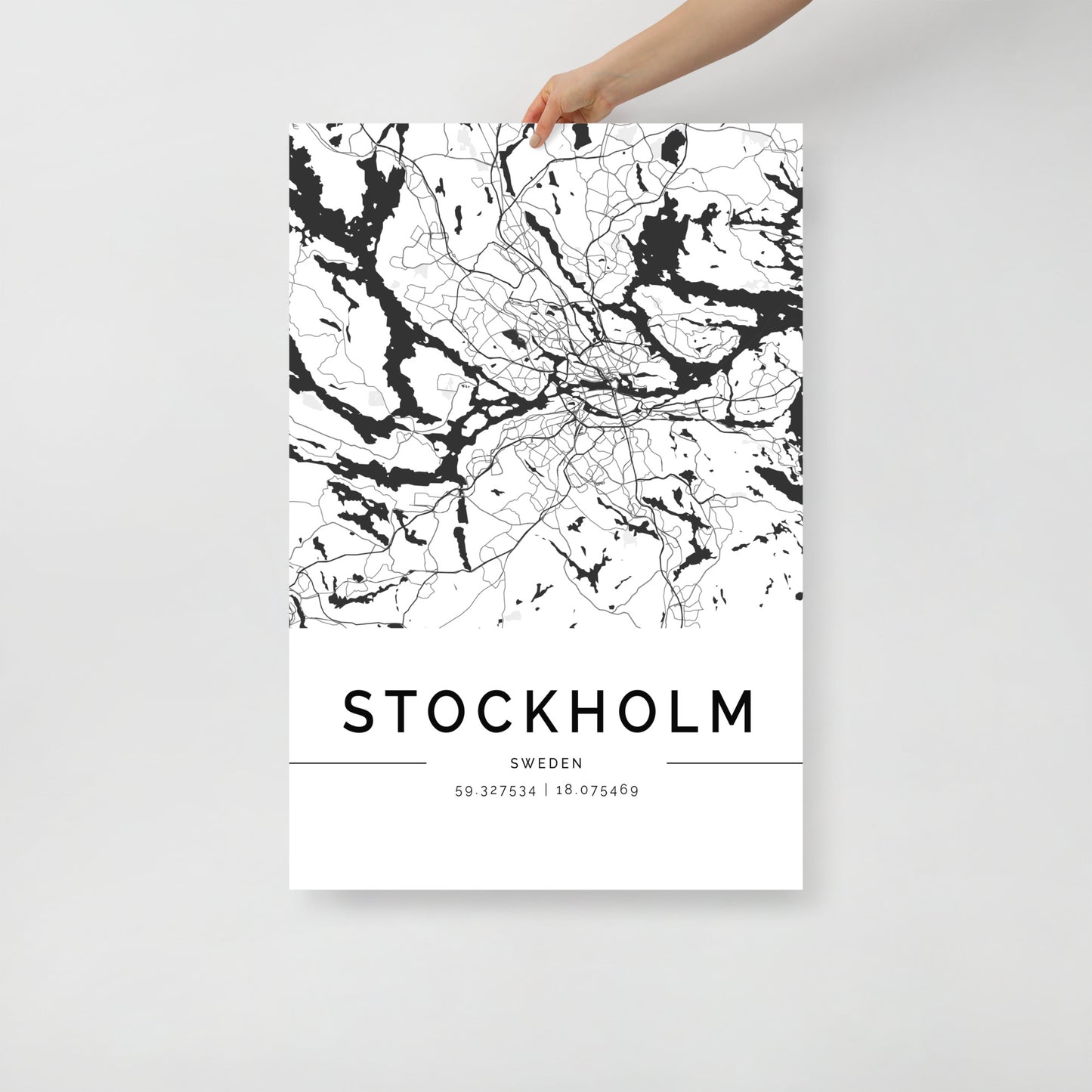 A person holds an FN Prints minimalist black-and-white Stockholm Map poster, showcasing geographic lines and waterways. This premium paper wall art includes the coordinates 59.327354 | 18.075469 at the bottom.