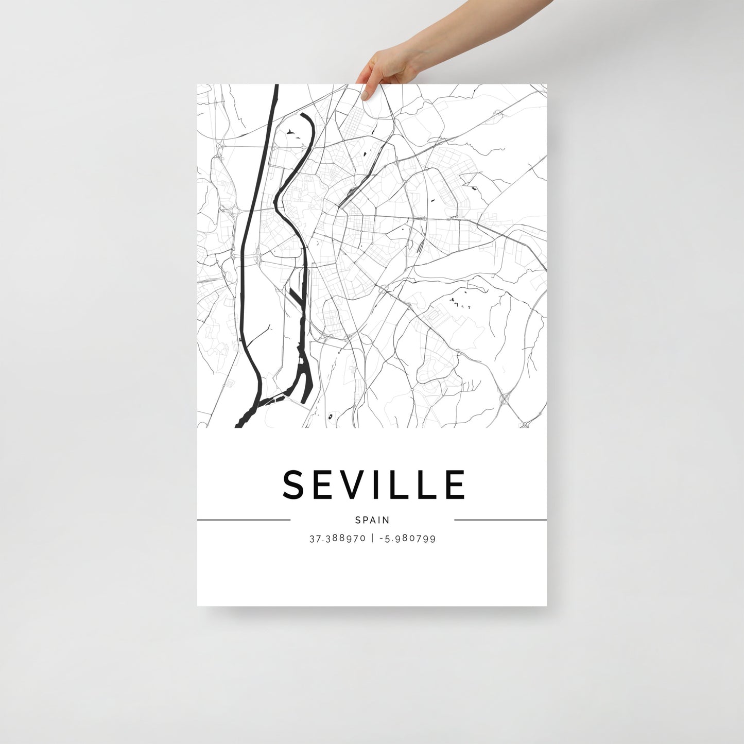 A hand showcases the FN Prints' Seville Map, a minimalist poster exquisitely printed on premium-grade paper, complete with geographic coordinates at the bottom. This stunning piece of wall art encapsulates the essence of Seville, Spain, through its sleek black and white design.