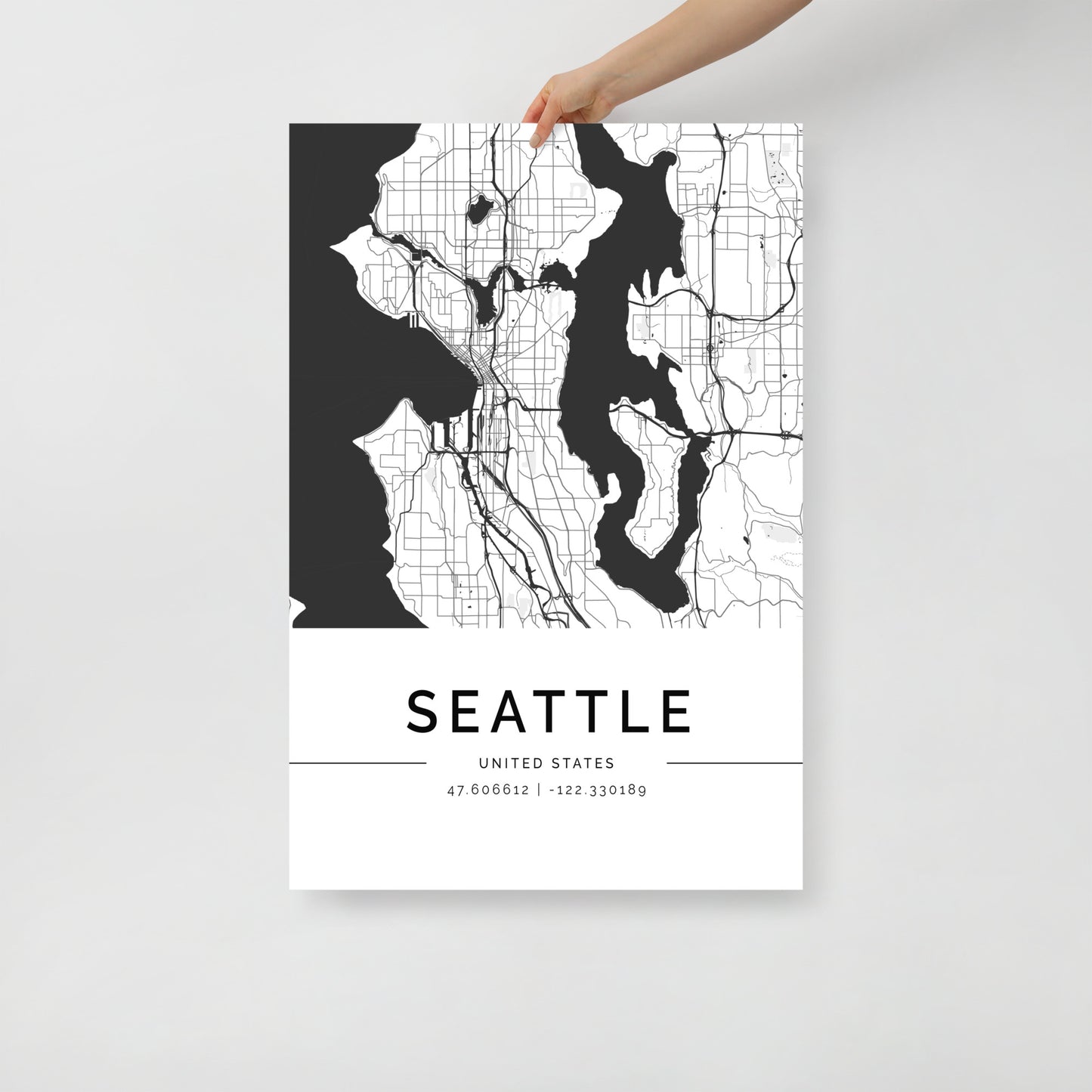 A person holds the Seattle Map by FN Prints, a minimalist poster crafted on premium-grade paper. This black and white artwork intricately showcases the streets and waterways of the urban landscape, with the city's name and geographical coordinates elegantly displayed at the bottom.