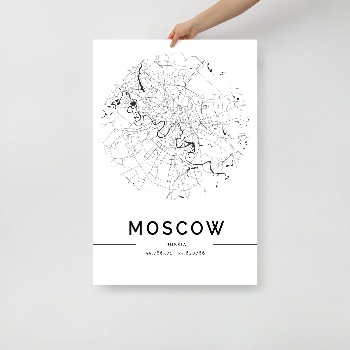 A hand holds an FN Prints Moscow Map poster, a minimalist black and white design that showcases the city's intricate urban layout with detailed street patterns. The map is elegantly labeled with "Moscow" and its coordinates (55.765698, 37.620769), highlighting the architectural beauty of Russia's capital.