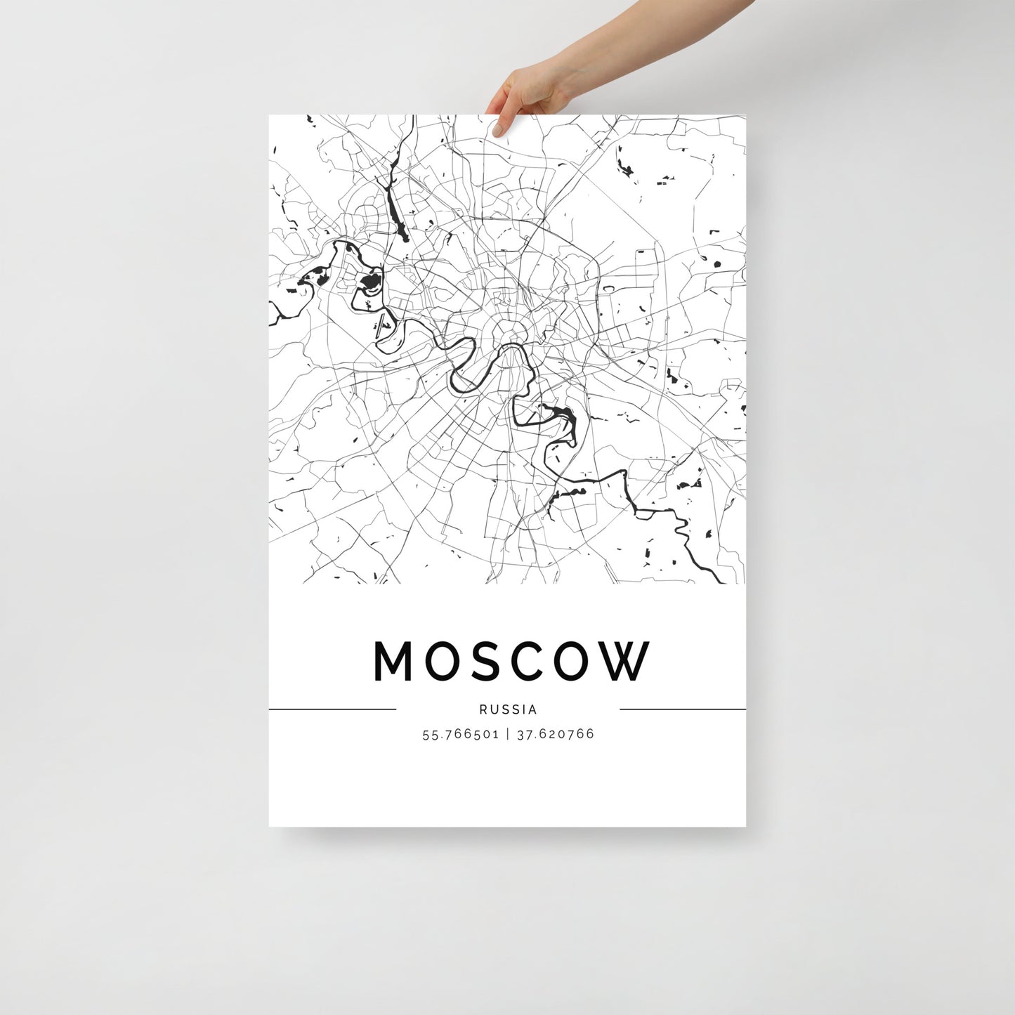 A person holds a detailed black and white Moscow Map poster by FN Prints, showcasing roadways and geographic markers. The city's name and coordinates are elegantly displayed at the bottom, highlighting its urban design and architectural beauty.