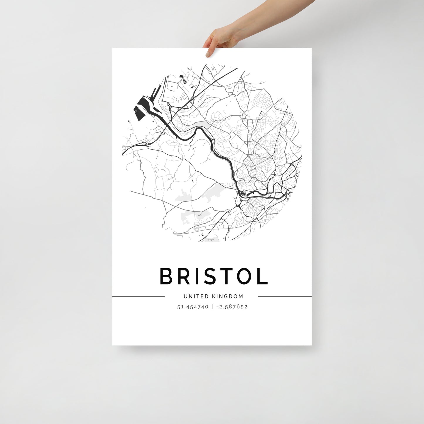 A hand displays a stunning black and white Bristol Map poster by FN Prints, highlighting the intricate urban layout of its historic streets. Detailed street lines and main roads are artfully woven across the print, with coordinates 51.454740, -2.587592 elegantly featured beneath the city's name.