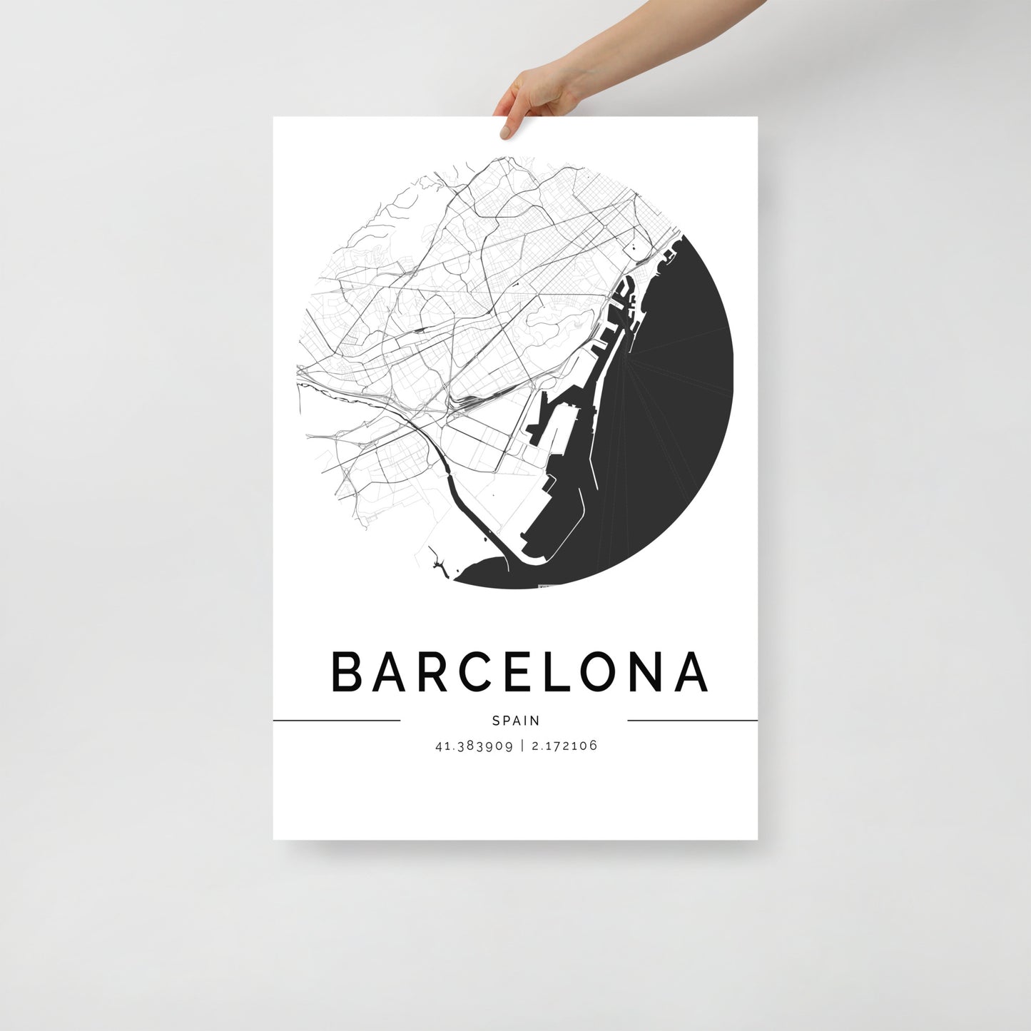 A person holds an eye-catching Barcelona Map poster by FN Prints, perfect for fans of urban design. This circular wall art showcases a stylized depiction of the city's layout and coastline, with its coordinates elegantly displayed beneath.