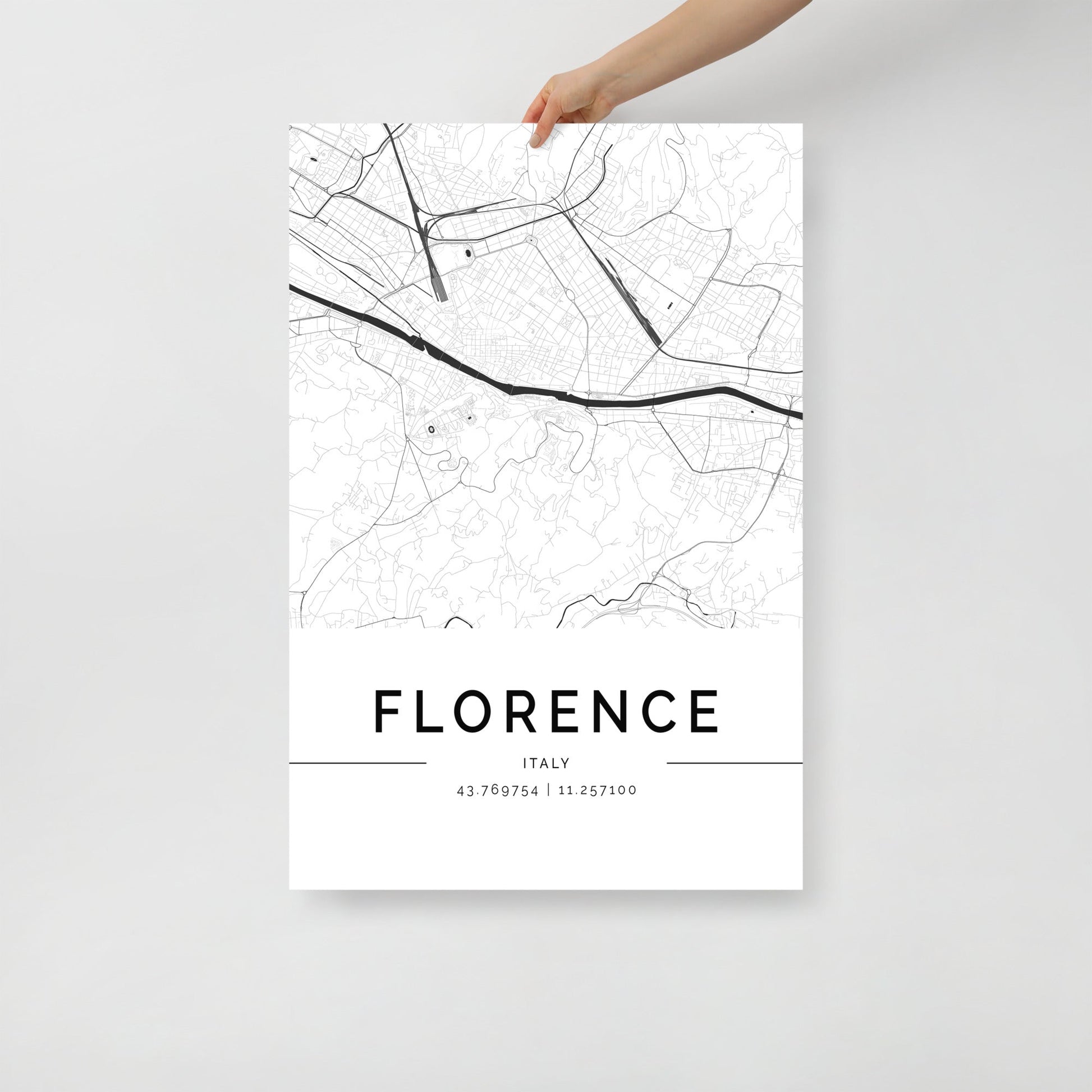 A hand displays an FN Prints "Florence Map" poster, ideal as wall art. This black and white print highlights the streets and a river of Florence, Italy, with the coordinates "43.769754 | 11.257000" featured below on a plain white background, beautifully capturing Italian essence.