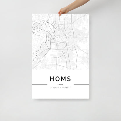 A person holds the Homs‎ Map by FN Prints, a stylish black and white city map poster of Homs, Syria. The print features geographic coordinates (34.734725 | 36.715547) elegantly placed below the city's name, with a plain white background that enhances its clean aesthetic.