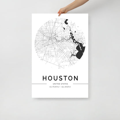 An individual holds the FN Prints "Houston City Map" poster, showcasing a circular, black and white design. It intricately details roads and geographical elements. The word "HOUSTON" along with the coordinates "29.763879, -95.383612" adorns the bottom, making it an ideal piece of wall art for any space.