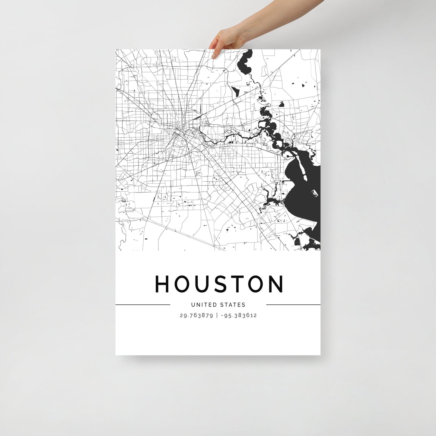 A person holds the elegant FN Prints Houston City Map, which features a stunning black and white design detailing street layouts, water bodies, and geographic coordinates (29.763879, -95.383162) on a crisp white background, perfectly capturing the essence of the city in sleek detail.