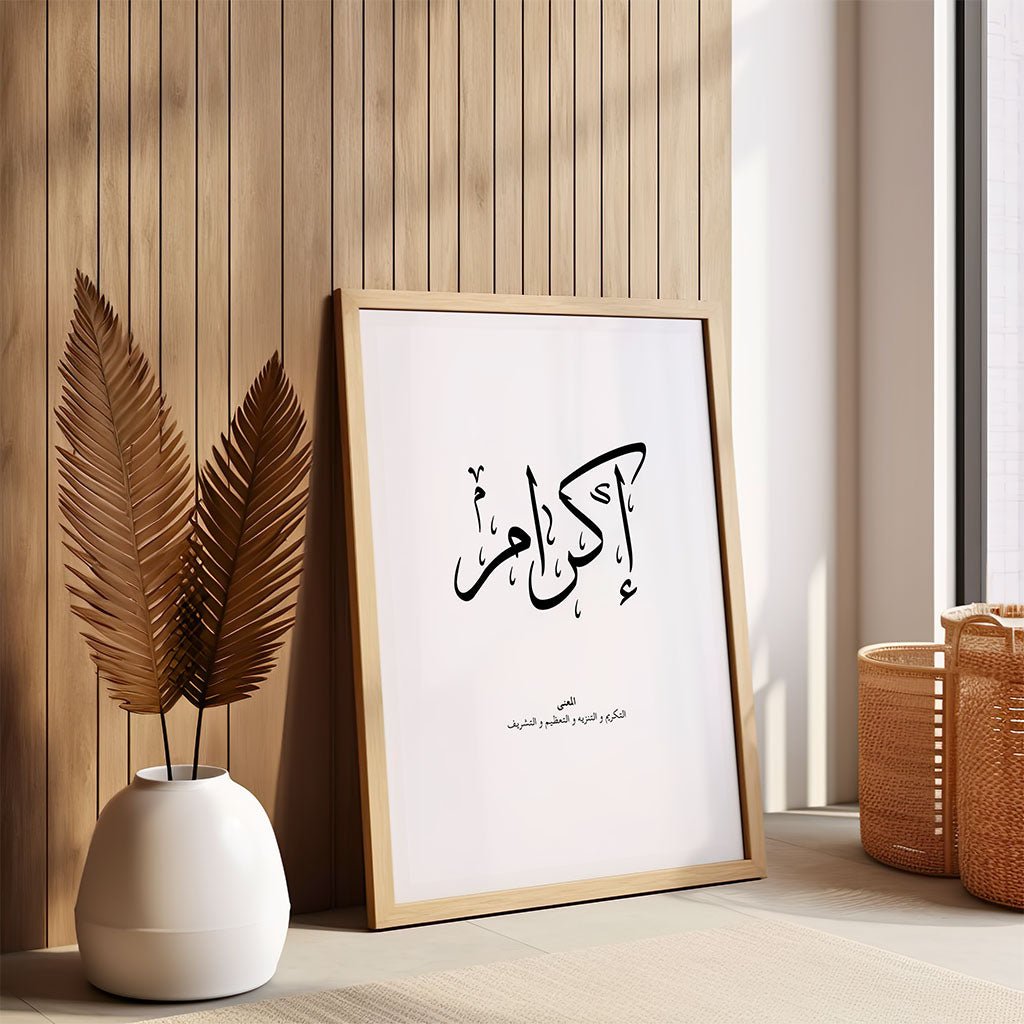 The Ikram - إكرام wall art by FN Prints, featuring Arabic calligraphy in a wooden frame, leans against a wood-paneled wall next to a white vase with dried leaves and two woven baskets, illuminated by sunlight from a nearby window.