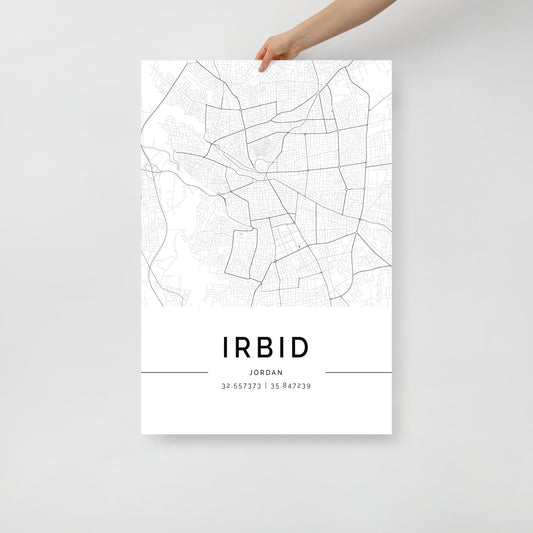 A hand showcases the FN Prints' Irbid City Map, a minimalist black and white wall art print representing Irbid, Jordan. The map highlights street lines and grids that embody the essence of Jordanian culture. Below, it features the text "IRBID, JORDAN" alongside the geographical coordinates "32.557373 | 35.847239".