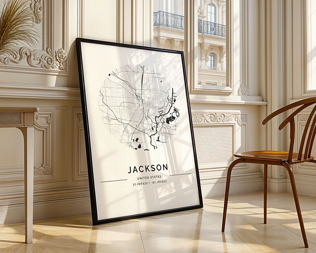 A framed FN Prints Jackson City Map leans against a sunlit wall, highlighting geographical details and coordinates. Its minimalist design complements the wooden chair and decorative molding, while a street view is visible through large windows.