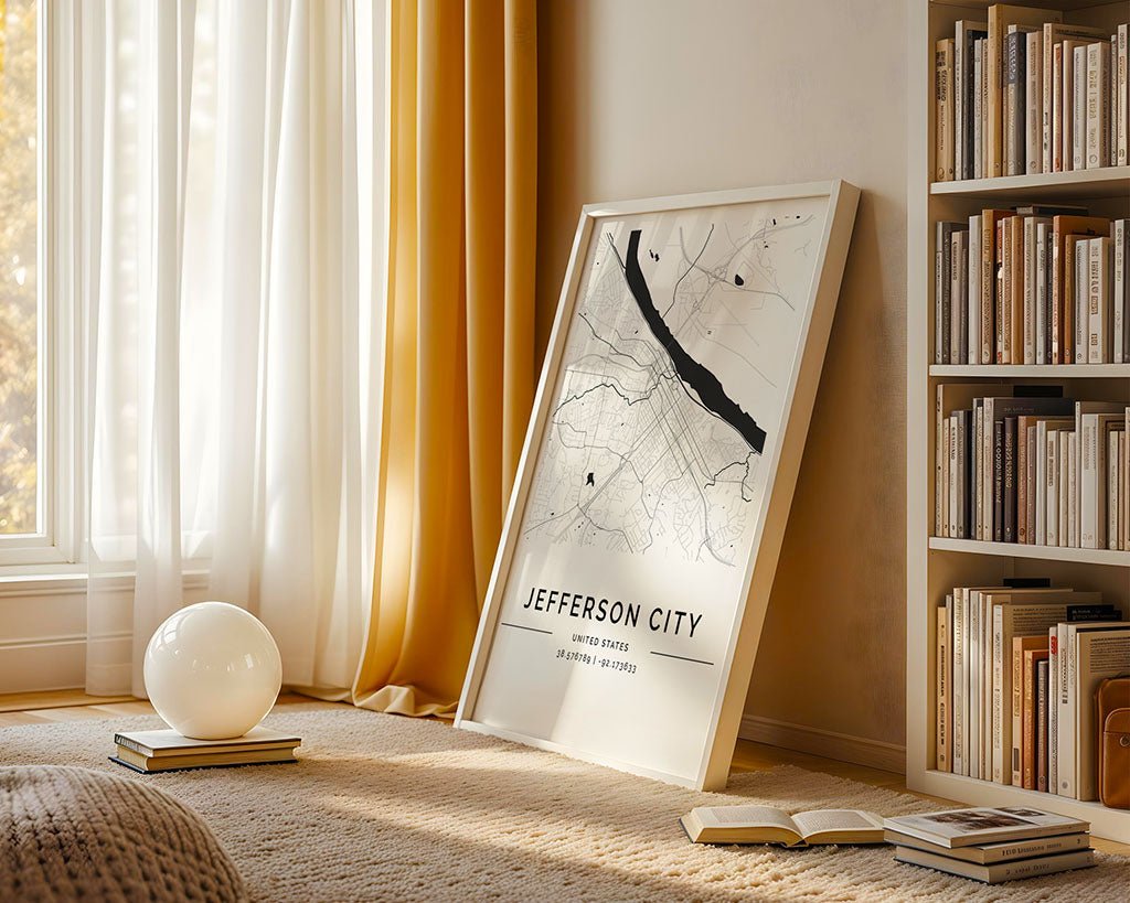 Sunlight streams through mustard sheer curtains in a cozy room. A large FN Prints Jefferson City Map leans against the wall, adding city wall art flair. A round white lamp and books complement the minimalist style, with a bookshelf filled with more books in the background.