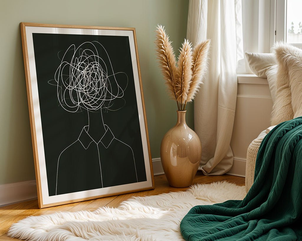 The framed "Jumbled Mind" abstract portrait by FN Prints, depicting mental turmoil, leans against a green wall. Nearby, a large beige vase with pampas grass graces a fluffy white rug. A green blanket covers a white couch by a window with sheer curtains.