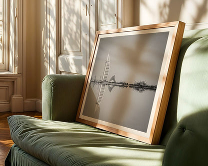 A framed photograph titled "Jumeriah Icons" from FN Prints, showcasing a black and white cityscape with Dubai's iconic sail-shaped skyscraper, reminiscent of the Burj al Arab, is propped on a green sofa. Sunlight streams through nearby windows, creating shadows on the wall and floor.