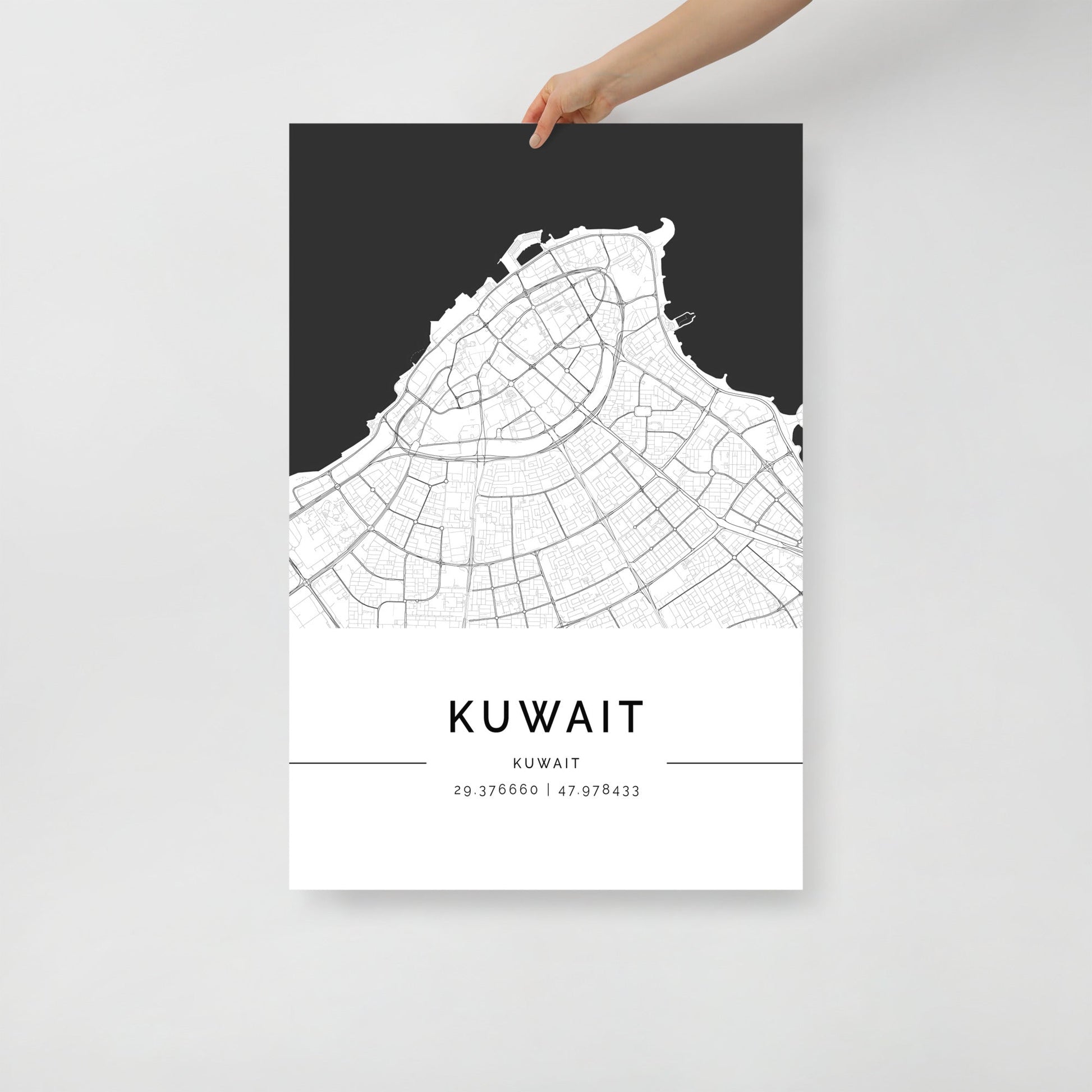 A hand holding a black and white map poster of Kuwait City.