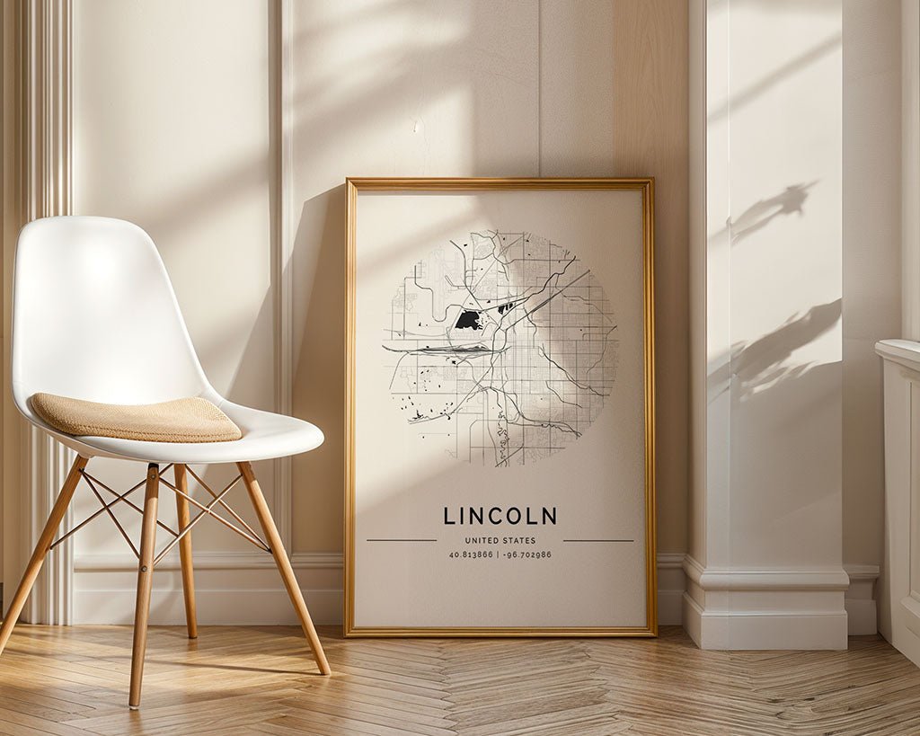 The FN Prints Lincoln City Map, a minimalist black-and-white framed print, rests on a wooden floor against a light wall. A nearby white chair with a cushion adds to the inviting atmosphere as sunlight casts warm shadows over the museum-quality paper.