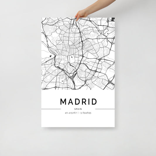 A hand is holding up a Madrid City Map from FN Prints, a stunning piece of black and white wall art. The urban design beautifully showcases the streets and geographical features, with the coordinates "40.4158671, -3.694695" alongside the city name "Madrid" displayed below the map.