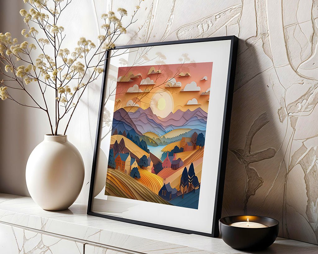 The framed digital art piece, "Mauve Mountains Sunset" by FN Prints, showcasing a vibrant countryside scene with hills, houses, and clouds, rests on a mantel beside a beige vase filled with dried flowers and a lit candle.