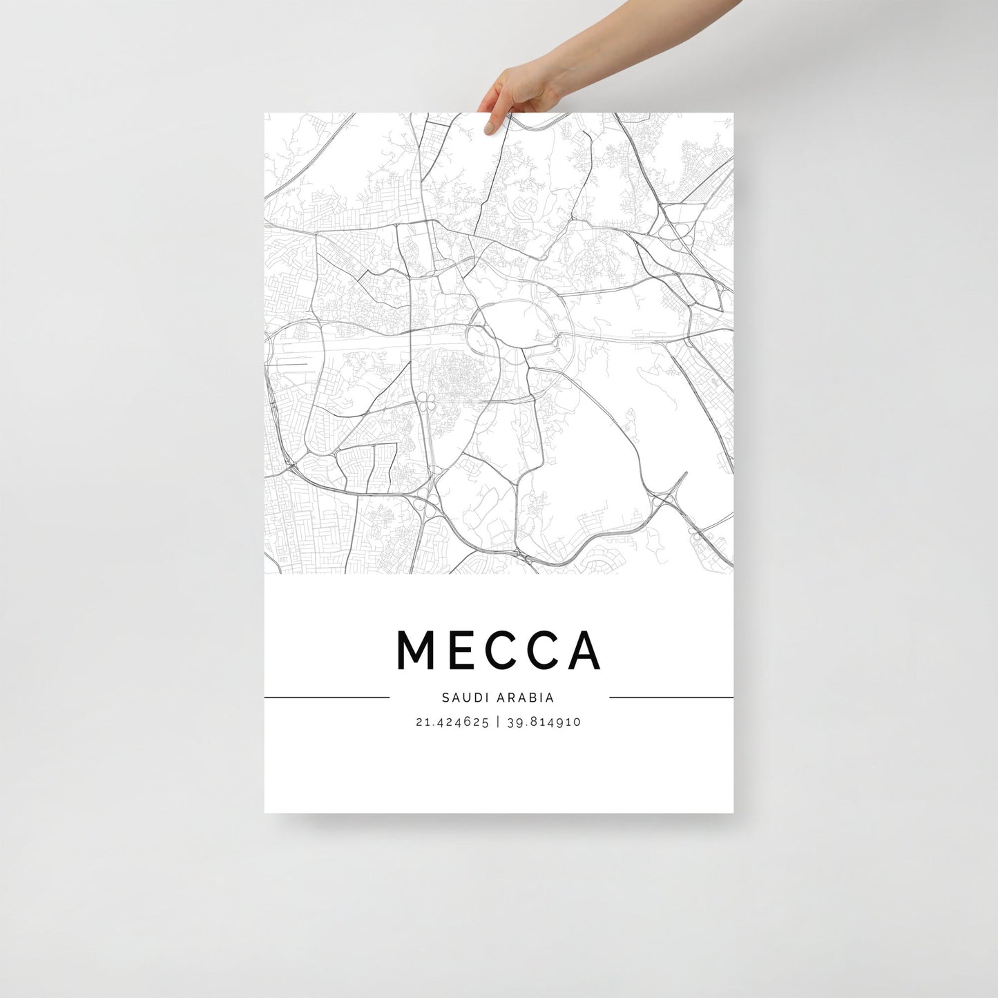 A person holds a breathtaking wall art print by FN Prints, featuring an intricate black and white city map poster of Mecca, Saudi Arabia. The coordinates 21.4240525 | 39.814910 are elegantly displayed beneath this Mecca City Map.