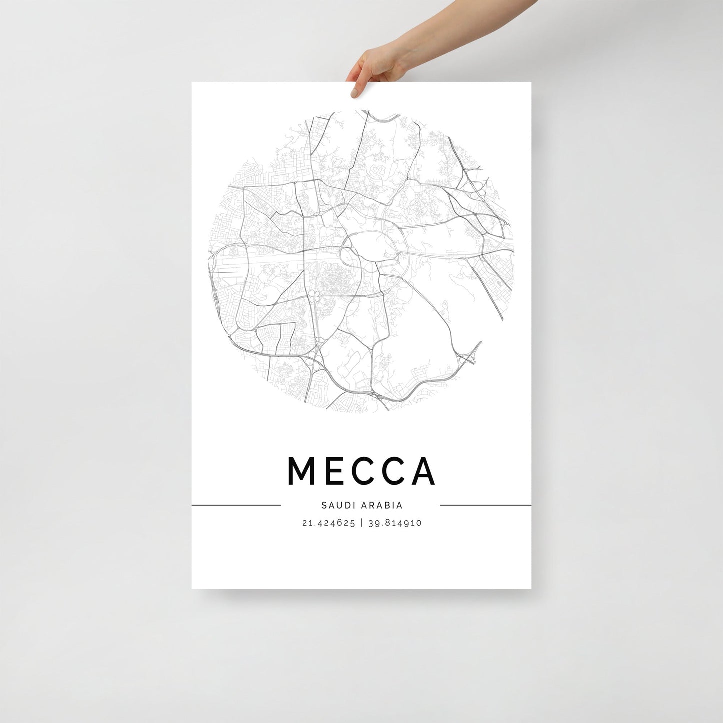 A hand holding the FN Prints "Mecca Map," a minimalist black and white Wall Art Print that highlights the geographical coordinates of Mecca at the bottom, paying homage to this sacred city's historical significance.